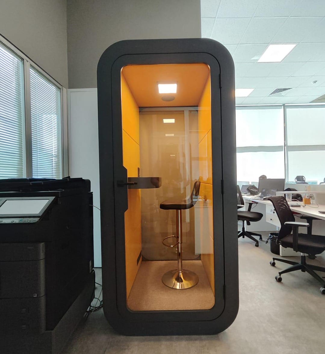Black phone booth with warm orange interior lit up in an office